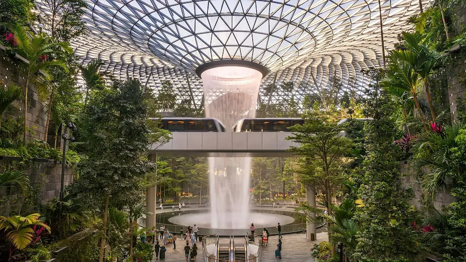 «آبشار سرپوشیده Jewel Changi در فرودگاه چانگی سنگاپور، احاطه‌شده با فضای سبز و قطار شهری»